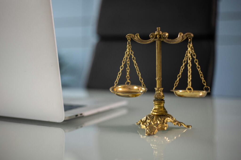 pexels-photo-6077797-6077797 Golden justice scales on a desk beside a laptop, symbolizing law and balance.