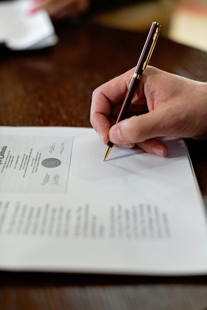 pexels-photo-8730982-8730982 A detailed close-up photo of a hand signing a formal document with a pen, creating a professional agreement.